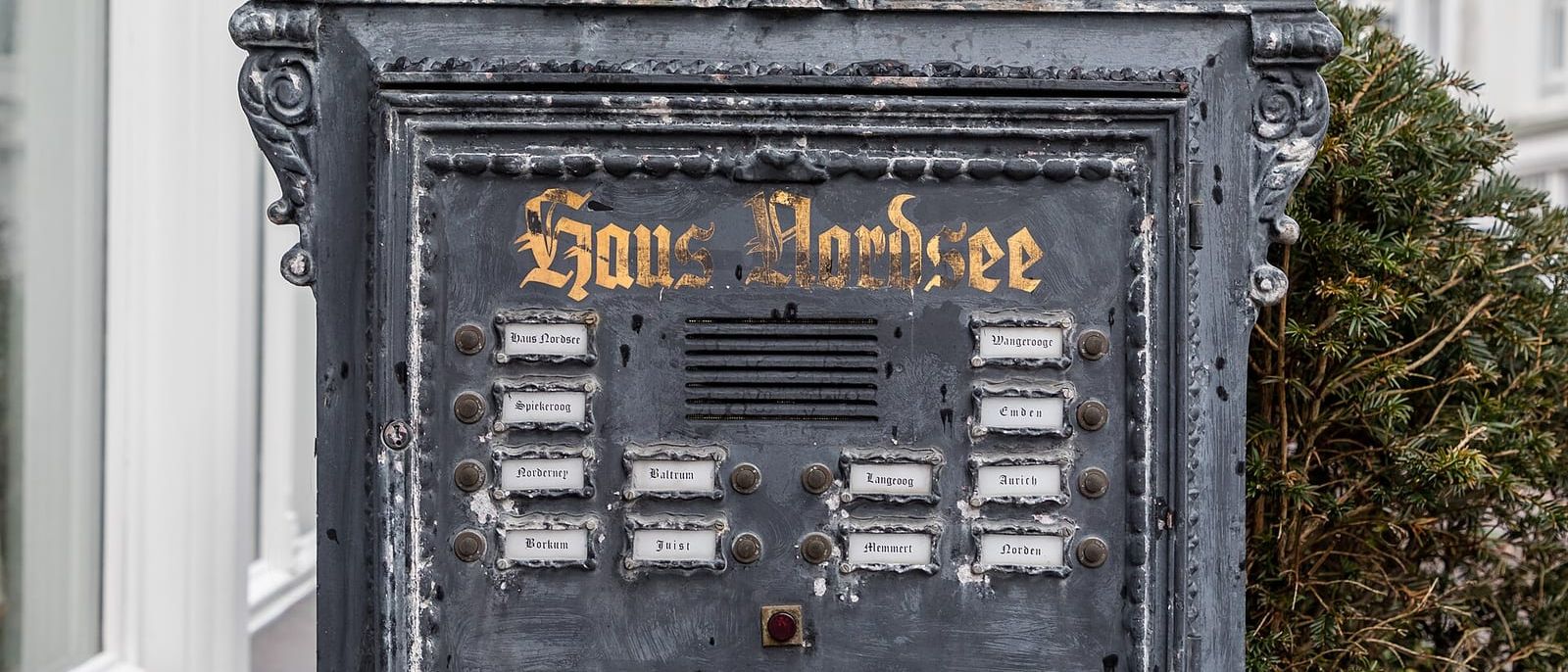 Alte gusseiserne Klingeltafel mit beschrifteten Namensschildern vor einem Haus auf Norderney