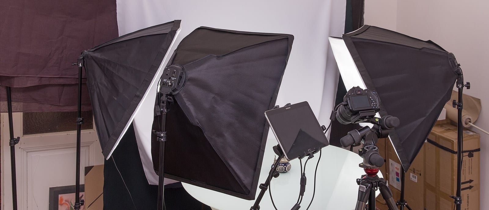 Kleines Fotostudio mit drei Softboxen, Kamera auf Stativ und weißem Hintergrund