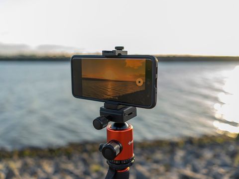 Smartphone auf einem Stativ filmt einen Sonnenuntergang am Wasser, Display im Fokus