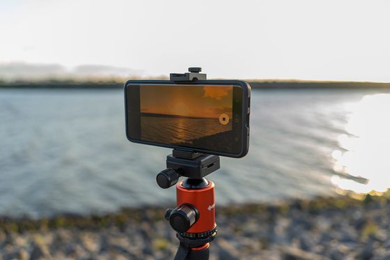 Smartphone auf einem Stativ filmt einen Sonnenuntergang am Wasser, Display im Fokus
