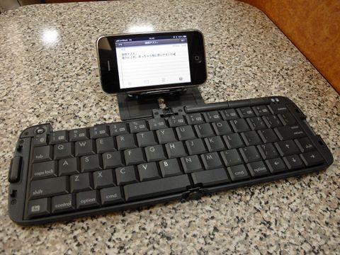 Klappbare Bluetooth-Tastatur auf einem Steintisch, dahinter ein Smartphone mit geöffneter Notiz