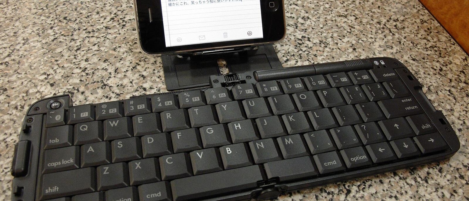 Klappbare Bluetooth-Tastatur auf einem Steintisch, dahinter ein Smartphone mit geöffneter Notiz