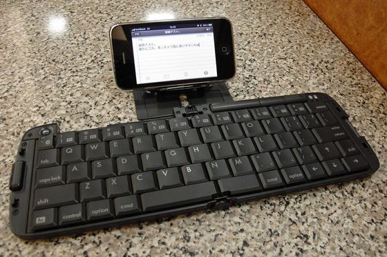 Klappbare Bluetooth-Tastatur auf einem Steintisch, dahinter ein Smartphone mit geöffneter Notiz